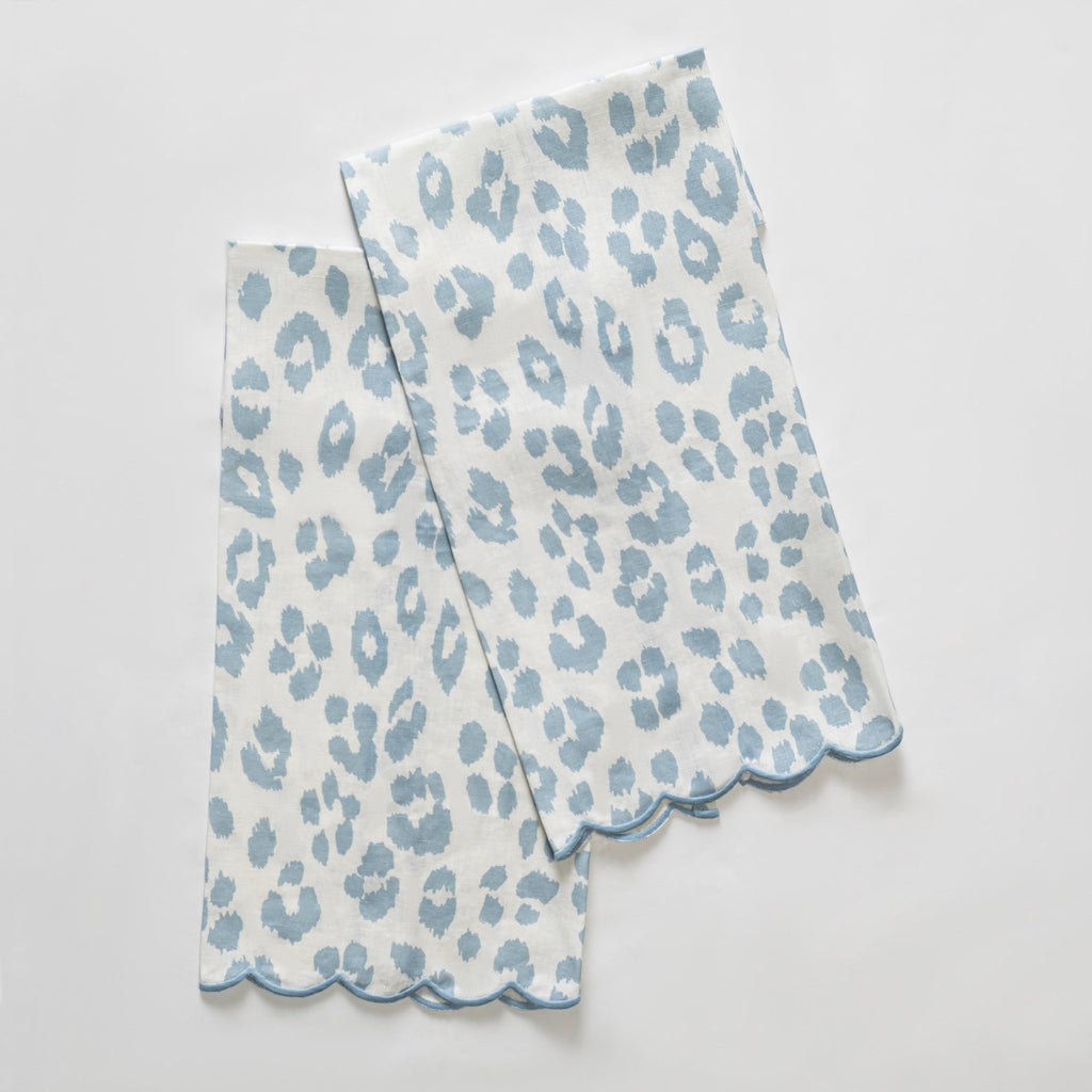 Matouk Schumacher Iconic Leopard Guest Towels in Sky blue animal print on white linen background and blue embroidered scallop edge