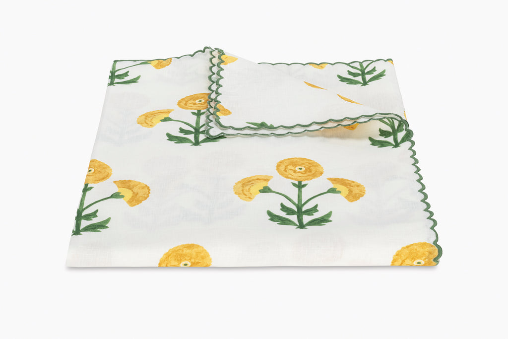 Matouk Gisele Tablecloth in Marigold Yellow with a white linen background and yellow and green block print flowers and green thread embroidered scallop edge