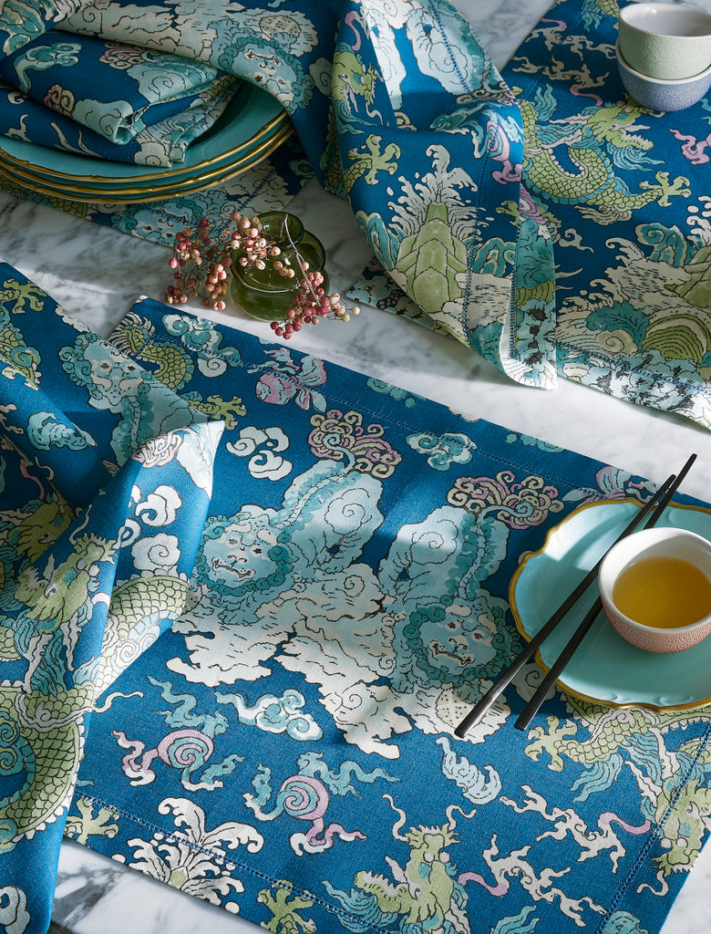 Matouk Schumacher Magic Mountain Napkins and Placemats in Aquarius features an aqua linen background with blue and green mythical creature print