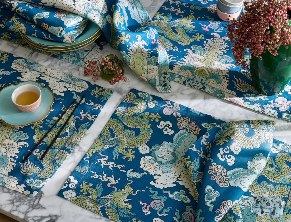 Matouk Schumacher Magic Mountain Napkins and Placemats in Aquarius features an aqua linen background with blue and green mythical creature print