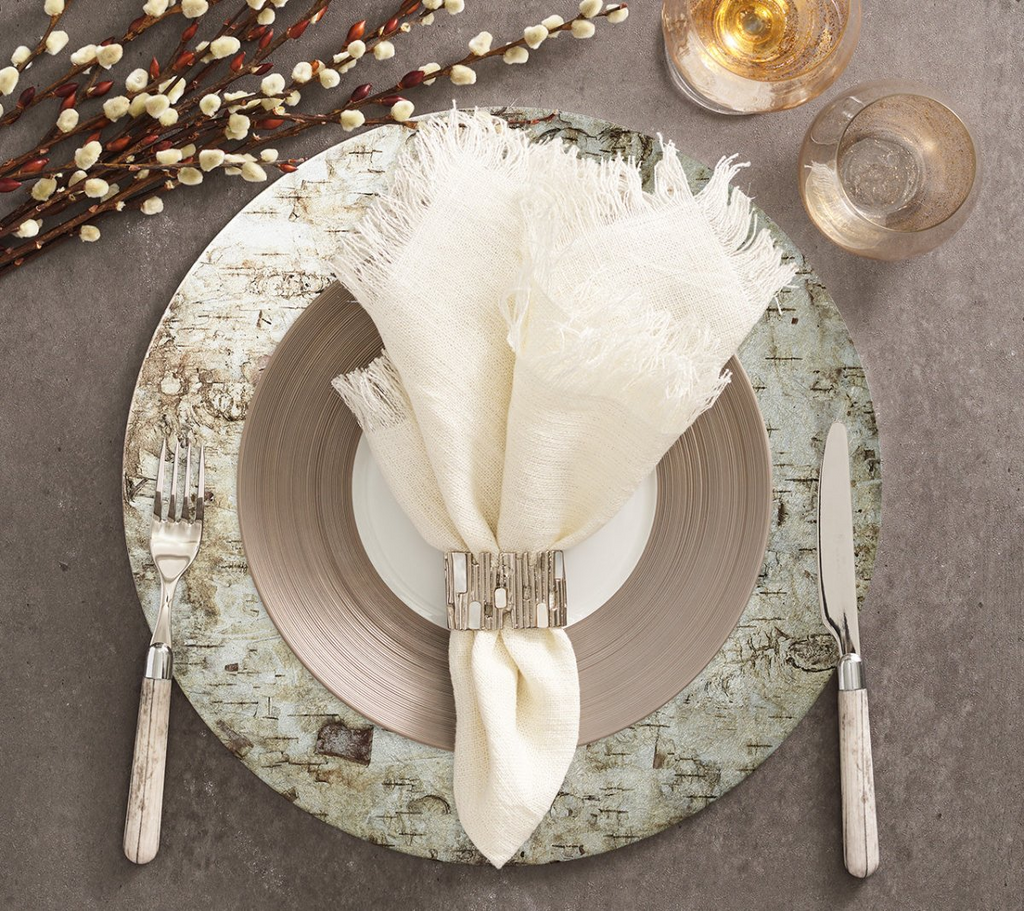 Elevate your table setting with the Chalet Placemat in Natural & Silver from Kim Seybert. The rustic birch bark image transferred onto a shimmering silver foil lacquered surface adds a touch of nature-inspired charm to any meal. Perfect for country or upscale settings, this placemat adds sophisticated, bucolic elegance to your dining experience.